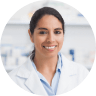 Smiling female healthcare provider in a white coat standing in a clinical environment, looking directly at the camera."