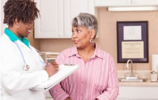 Senior woman speaking with a female doctor in a clinical office, both smiling and holding a friendly conversation.